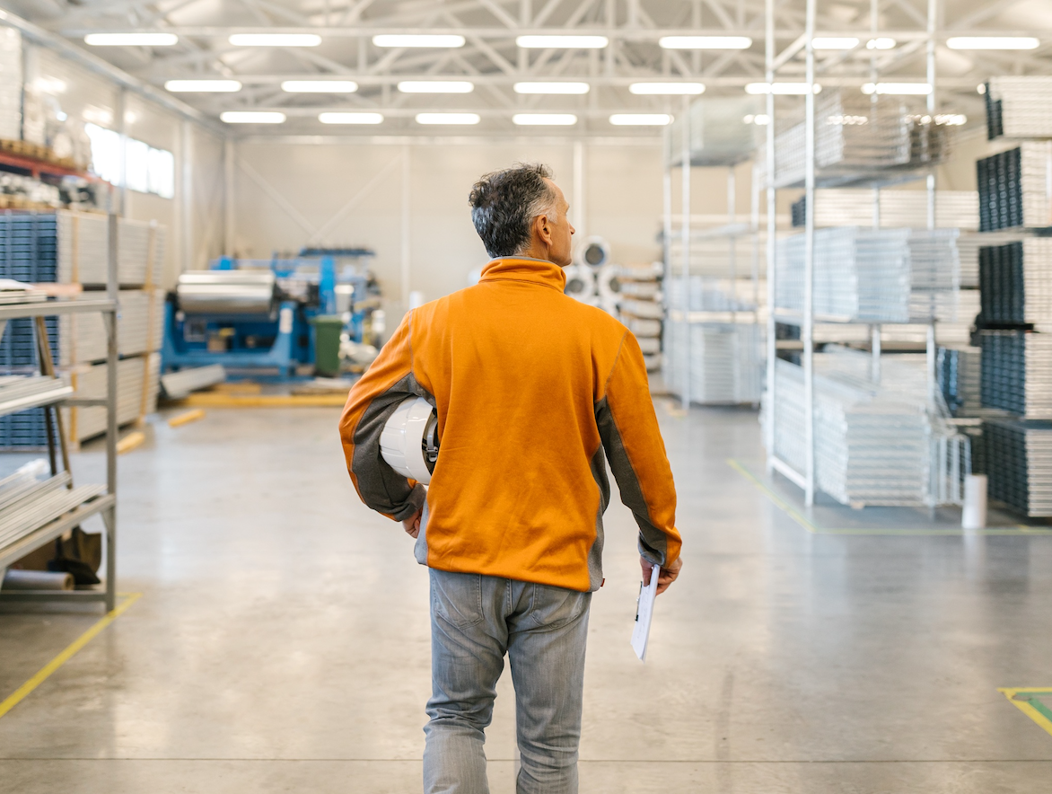 Back shot of a senior male worker holding a clipboard ready to start an inspection of a production in a factory storage.